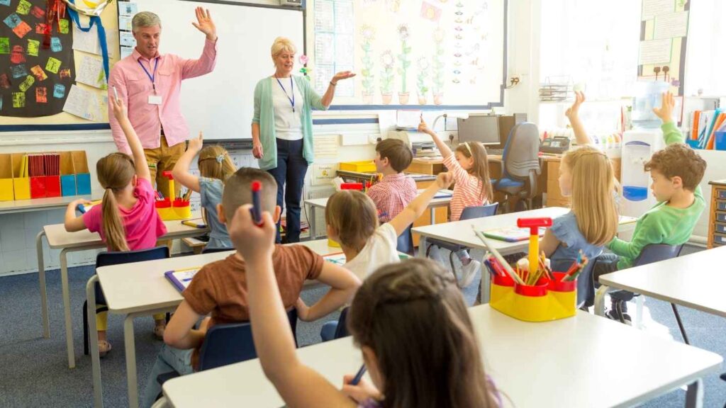 Children raising their hands during a classroom discussion with teachers.